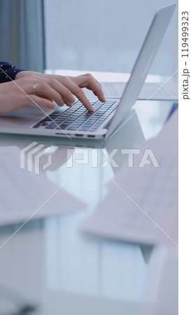 Business woman is working with laptop computer while sitting at the glass table in home office, closeup of hands Business woman is working with laptop computer while sitting at the glass table in home office, closeup of hands 119499323