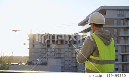 Man constructive engineer with white hard hat and safety vest is using a tablet computer while inspecting a construction site at sunset Man constructive engineer with white hard hat and safety vest is using a tablet computer while inspecting a construction site at sunset 119499380