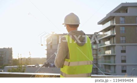 Male engineer with white hard hat and safety vest is using a tablet computer while inspecting a construction site at sunset Male engineer with white hard hat and safety vest is using a tablet computer while inspecting a construction site at sunset 119499404