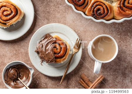 Chocolate swirl buns with hazelnut chocolate filling. Chocolate cinnamon buns and coffee served for breakfast on brown background top view 119499563