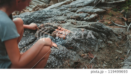 Woman making seafood barbeque sit on rocks on sea cost. Evening time, dark toning. Cooking shrimps on open fire. Leisure, food, people. Outdoor lifestyle travel summer holiday vacation. Slow Woman making seafood barbeque sit on rocks on sea cost. Evening time, dark toning. Cooking shrimps on open fire. Leisure, food, people. Outdoor lifestyle travel summer holiday vacation. Slow 119499693