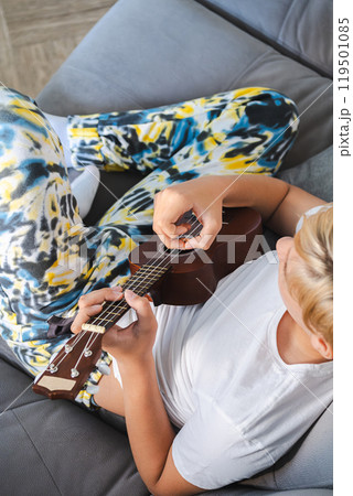 Teen boy playing ukulele, enjoying music. 119501085