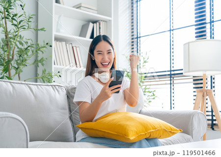 Happy young asian woman relax on comfortable couch at home texting messaging on smartphone 119501466