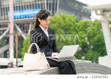 屋外でスーツ姿でノートパソコンで作業する若いビジネスウーマン 屋外でスーツ姿でノートパソコンで作業する若いビジネスウーマン 119502561