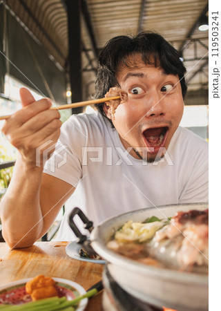 Happy and excited face man eating Moo Kra Ta or Thai BBQ buffet. 119503241