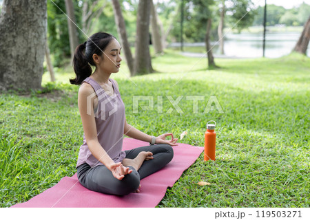 Young Woman Practicing Yoga Outdoors in a Serene Park Setting, Relaxing and Meditating on a Pink Yoga Mat Surrounded by Nature 119503271