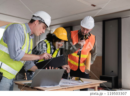 Engineering Team Collaborates on Work Plan at Construction Site with Safety Gear and Blueprints 119503307