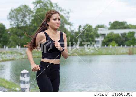 Fit Young Woman Jogging Outdoors by a Scenic Lake on a Cloudy Day, Embracing a Healthy Lifestyle and Staying Active Fit Young Woman Jogging Outdoors by a Scenic Lake on a Cloudy Day, Embracing a Healthy Lifestyle and Staying Active 119503309