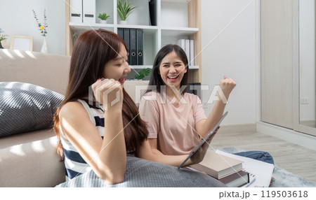 Young Women Celebrating Success in Online Studies at Home with Laptop and Books, Expressing Joy and Achievement Young Women Celebrating Success in Online Studies at Home with Laptop and Books, Expressing Joy and Achievement 119503618