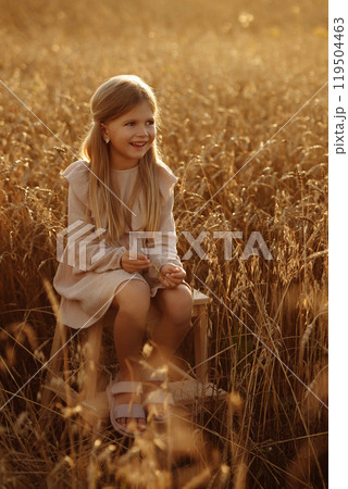 A young blonde girl in a beige dress sits in a field with tall grass. A young blonde girl in a beige dress sits in a field with tall grass. 119504463
