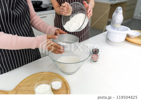 Hand sifting flour in a kitchen with baking ingredient, colorful icing and electric mixer on the side. 119504825