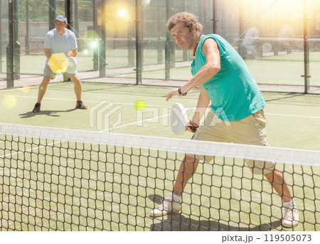 Four men practice playing padel on an outdoor court 119505073
