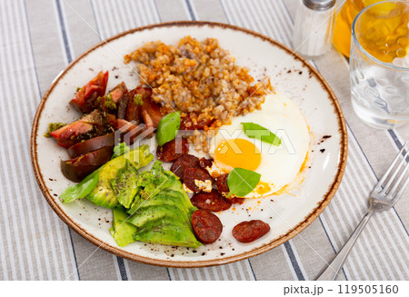 Delicious breakfast made from buckwheat, sun-dried tomatoes, avocado, fried eggs with basil and hunting sausages Delicious breakfast made from buckwheat, sun-dried tomatoes, avocado, fried eggs with basil and hunting sausages 119505160