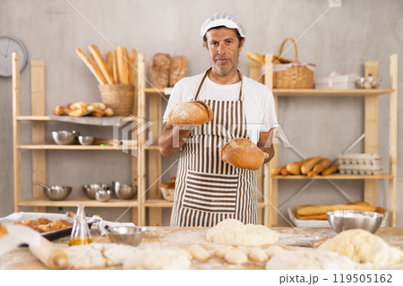 Portrait of baker holding tasty hot bread and baguettes in hands in kitchen 119505162