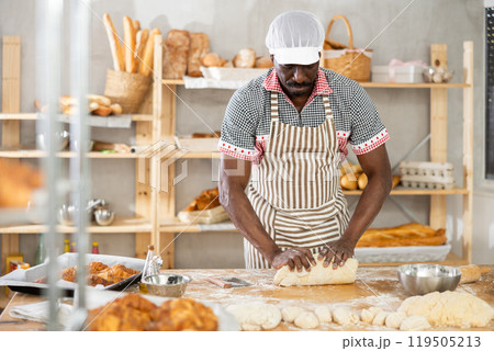 Experienced black baker kneading dough in artisan bakery Experienced black baker kneading dough in artisan bakery 119505213