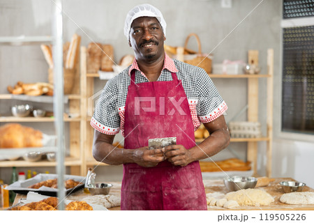 Smiling baker standing in bakery with dough scraper in hands Smiling baker standing in bakery with dough scraper in hands 119505226