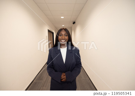 In a contemporary office hallway, a selfassured female business professional is smiling In a contemporary office hallway, a selfassured female business professional is smiling 119505341