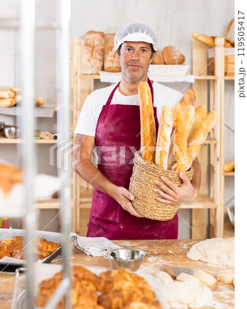 Caucasian male cook-baker worker with basket of baguettes, shows many products 119505417