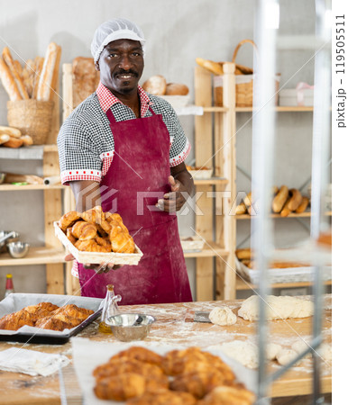 Smiling African baker offering freshly baked croissants in bakery Smiling African baker offering freshly baked croissants in bakery 119505511