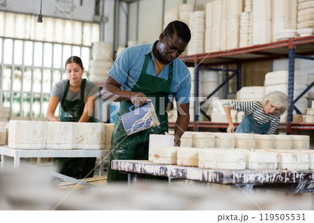 Slip casting - african american worker pours slip mass from jug into plaster mold in pottery factory 119505531