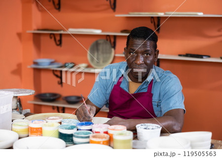 Male craftsman painting clay plates acrylic paints in art studio 119505563