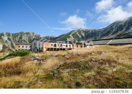Murodo, Tateyama Kurobe Alpine Route, Japan, A serene landscape featuring a rustic building surrounded by mountains and grassy fields under a blue sky with wispy clouds. Murodo, Tateyama Kurobe Alpine Route, Japan, A serene landscape featuring a rustic building surrounded by mountains and grassy fields under a blue sky with wispy clouds. 119507636