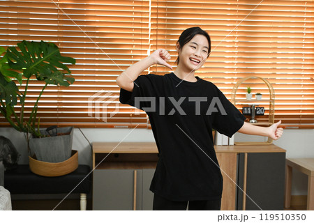 Cheerful young asian woman having fun, practicing a dance move in a living room Cheerful young asian woman having fun, practicing a dance move in a living room 119510350