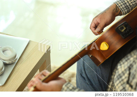 Young man playing an acoustic guitar while sitting on sofa at home. Leisure activity and hobby concept Young man playing an acoustic guitar while sitting on sofa at home. Leisure activity and hobby concept 119510368
