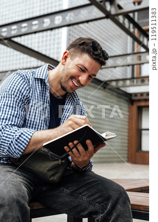 A person writes in a notebook while sitting on a park bench 119511383