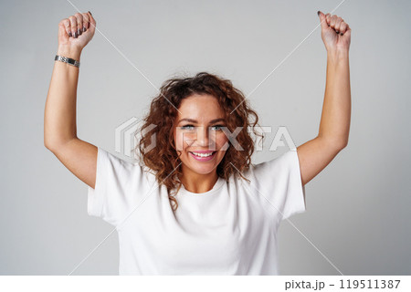 Young woman joyfully celebrates in casual attire against a neutral background Young woman joyfully celebrates in casual attire against a neutral background 119511387