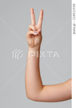 A hand showing the peace sign against a simple gray background 119511530