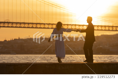 Couple holding hands and dancing by river at sunset Couple holding hands and dancing by river at sunset 119512273