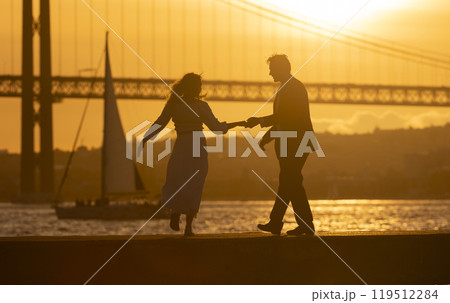 Couple holding hands and dancing by river at sunset 119512284