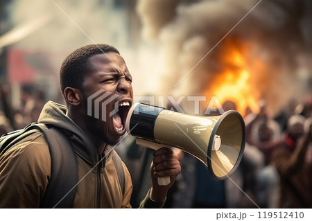 An angry African-American man yells into a megaphone amid and fire during the rally. 119512410