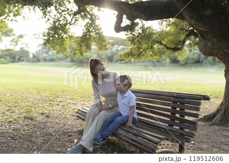 Mother and son relaxing on park bench in the sunlight 119512606