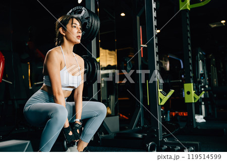 Asian woman holding and lifting a weight kettlebell in fitness gym, heavy kettle bell for strength training exercise in upper arm exercise to build muscle, Working out, healthy lifestyle concept 119514599
