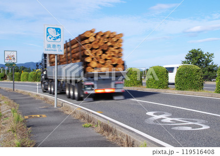木材を満載したトレーラー式の大型トラックが鳥取県境港市の米子鬼太郎空港沿いのメロディー道路を走る光景 119516408