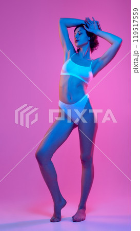 Woman posing elegantly with her arms raised, gracefully accentuating her curves in neon light against vibrant, colorful backdrop. Woman posing elegantly with her arms raised, gracefully accentuating her curves in neon light against vibrant, colorful backdrop. 119517559