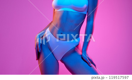 Woman in white underwear stands confidently, hands on hips, against vibrant pink backdrop with blue lighting, highlighting her toned physique. Woman in white underwear stands confidently, hands on hips, against vibrant pink backdrop with blue lighting, highlighting her toned physique. 119517597