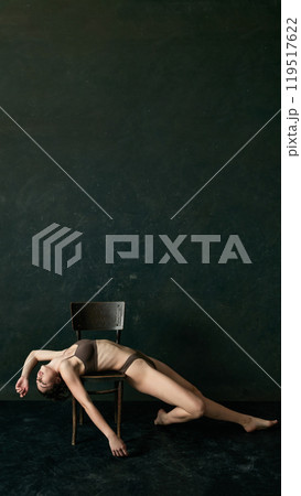 Poster. Beautiful woman drapes herself over chair, arms and legs extended, giving relaxed yet elegant feel in soft lighting. Copy space. Poster. Beautiful woman drapes herself over chair, arms and legs extended, giving relaxed yet elegant feel in soft lighting. Copy space. 119517622