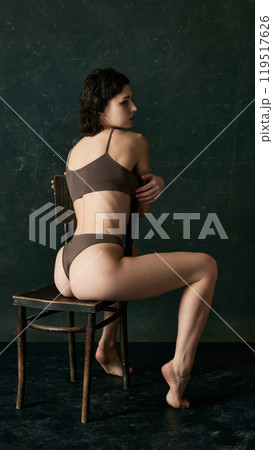 Rear view photo of young woman sitting on chair, and looking to side, light emphasizes natural curves of her back and shoulders. 119517626