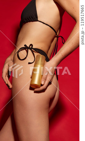 Close-up of woman holding gold skincare bottle against vivid red background. Attention to body care products and healthy skin. Close-up of woman holding gold skincare bottle against vivid red background. Attention to body care products and healthy skin. 119517665