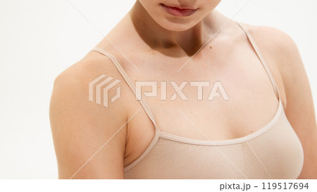 Close up photo of young woman in beige lingerie. Focus on breast, neckline against white studio background. Smooth and well-kept skin Close up photo of young woman in beige lingerie. Focus on breast, neckline against white studio background. Smooth and well-kept skin 119517694