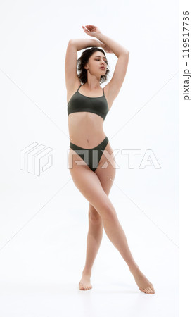 Model in dark green set posing, raising hands above head and looking away, exuding confidence and grace, against white background. Model in dark green set posing, raising hands above head and looking away, exuding confidence and grace, against white background. 119517736
