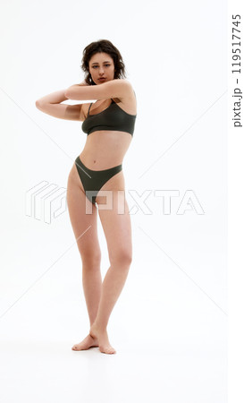 Full-length photo of young attractive woman posing in dark green lingerie and looking at camera, showing confidence against white studio background. Full-length photo of young attractive woman posing in dark green lingerie and looking at camera, showing confidence against white studio background. 119517745