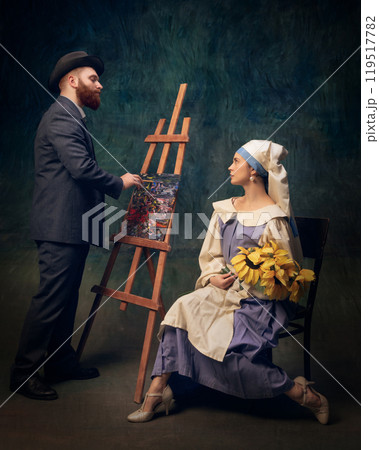Man dressed in vintage style painting on easel, while woman, holding sunflowers, watches in seated pose. 119517782
