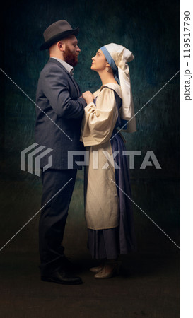 Cinematic full-length portrait of man in a suit and elegant woman in dress and headscarf standing closely to each other and holding hands. Cinematic full-length portrait of man in a suit and elegant woman in dress and headscarf standing closely to each other and holding hands. 119517790