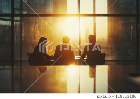 Sunset meeting in a corporate office with three professionals engaged in discussion against a golden Sunset meeting in a corporate office with three professionals engaged in discussion against a golden 119518186