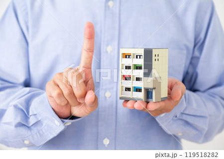 マンションの住宅模型を持って人差し指を立てるミドル男性 119518282