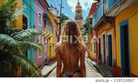 A woman in a bikini walks on a cobblestone street by colorful buildings 119518887